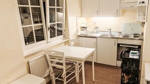 A compact kitchen with white cabinetry, a small dining table, and a window with curtains. - Studio Turmalin by Interhome (Leukerbad)