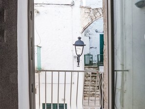 Blick durch ein Fenster mit weißer Wand, grünem Rollo und einem Metallgeländer.