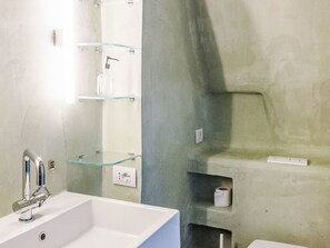 Ein Badezimmer mit einem weißen Waschbecken, einer Duschkabine aus Glas und einem Toilettenpapierhalter an der Wand.