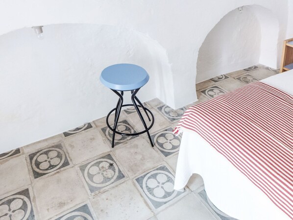 Ein Zimmer mit einem Bett, einem blauen Hocker und fußbodenhohen, gemusterten Fliesen.