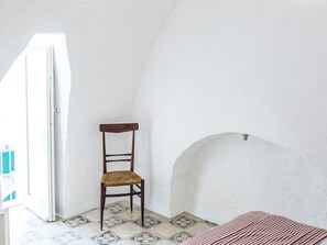 Ein Zimmer mit einem Sessel, gefliestem Boden und einer weißen Wand.