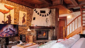 A cozy living room with a stone wall, a fireplace, a television, and a wooden staircase. - Mayens du Rudet by Interhome (Erde)