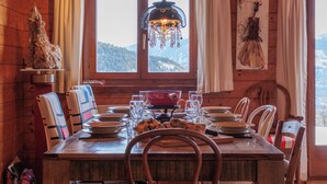 A wooden cabin dining area with a table set for four, a hanging light fixture, and a view of a snowy mountain landscape through a window. - Mayens du Rudet by Interhome (Erde)