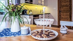 Una mesa de comedor con una cesta blanca llena de galletas, un jarrón blanco con flores y un mantel individual de estampado azul.
