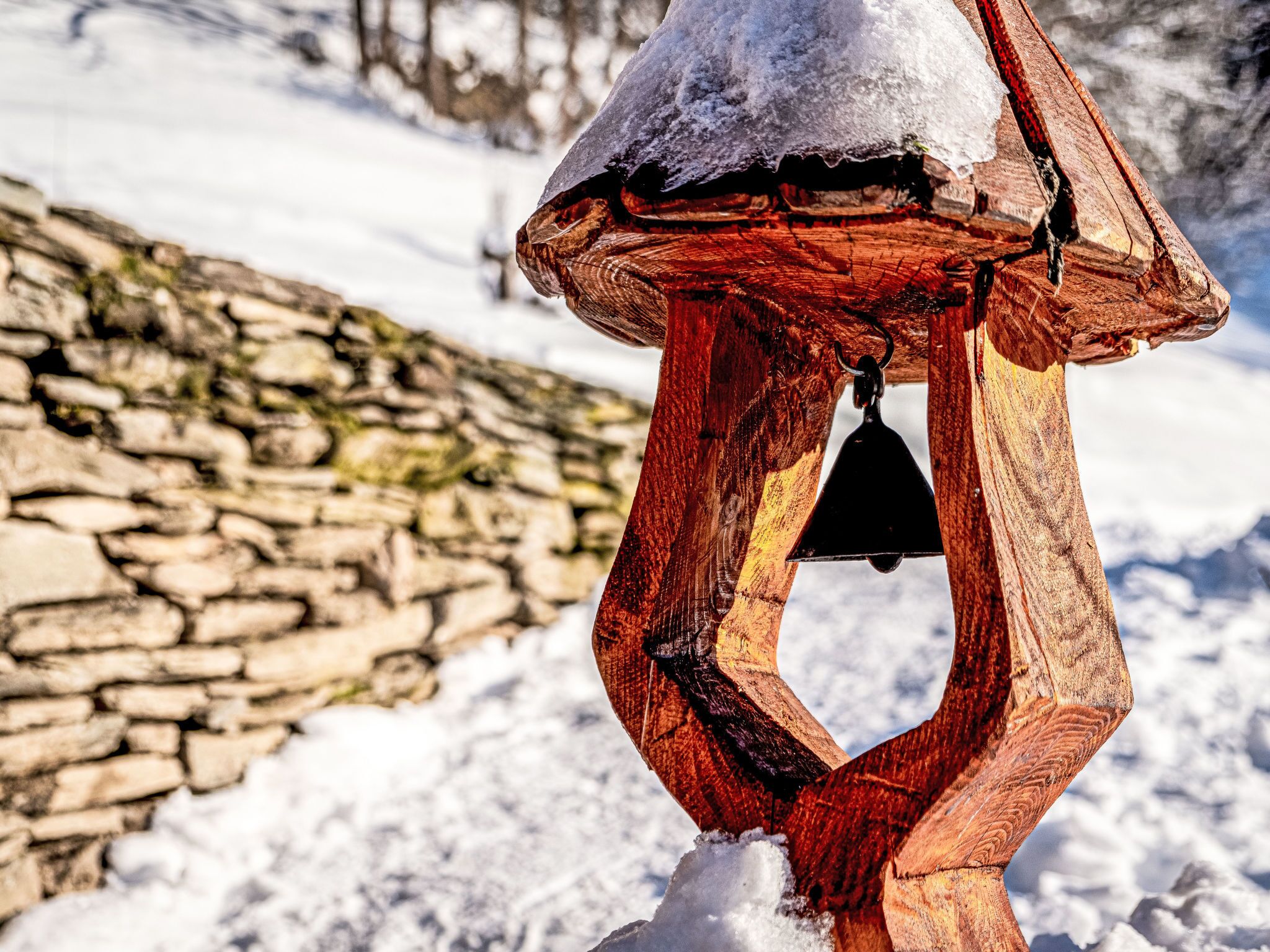 A wooden bell structure with a stone wall in the background.