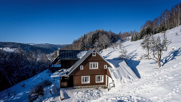 Una cabaña de madera con techo inclinado, un balcón y vistas a un valle cubierto de nieve.