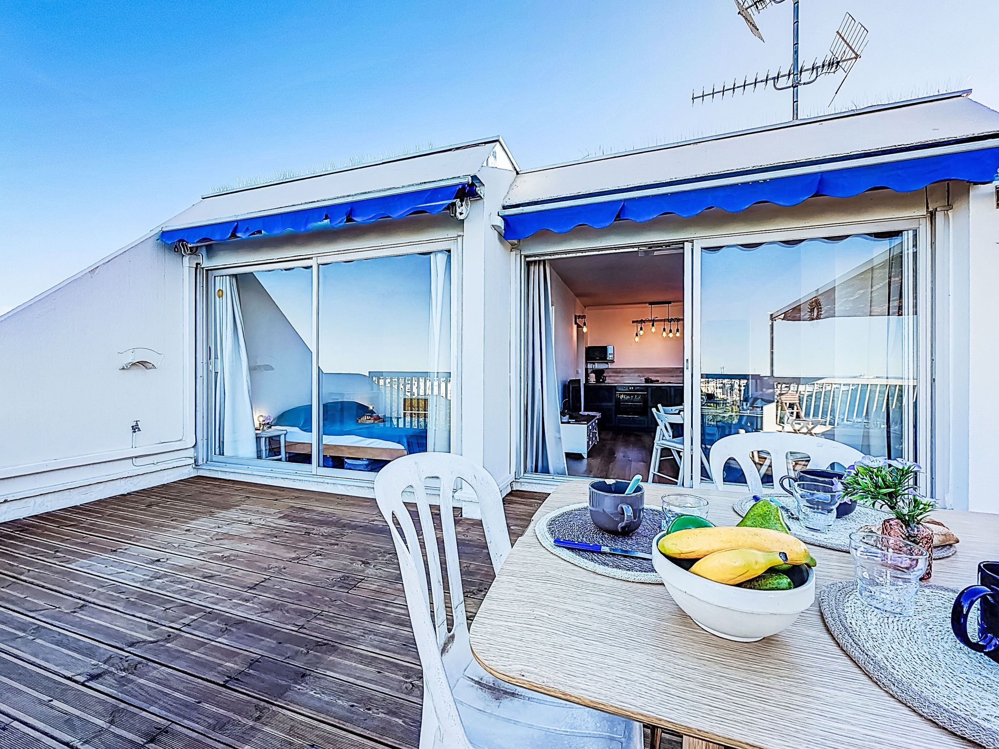 A deck with a table set for breakfast, a chair, and a view of the interior of the building.