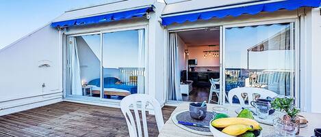 A deck with a table set for breakfast, a chair, and a view of the interior of the building.