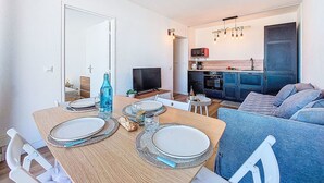 En matplats med ett bord dukat för två personer, ett kök med moderna vitvaror och ett vardagsrum med en soffa.