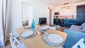 En matplats med ett träbord dukat för två personer, en tv och ett litet kök i bakgrunden.