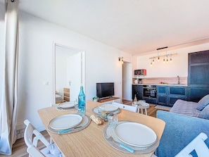 Een eethoek met een houten tafel gedekt voor twee personen, een televisie en een kitchenette op de achtergrond.