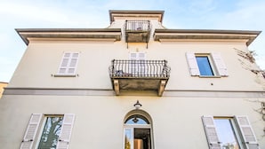 Un immeuble de deux étages doté d’un balcon, d’une entrée centrale surmontée d’une arche et de volets aux fenêtres.