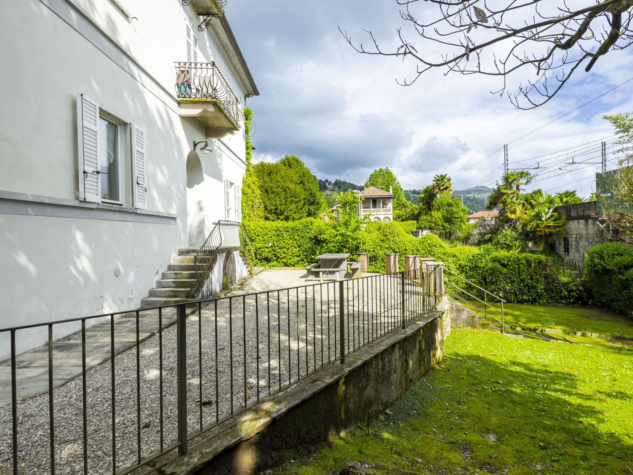 A white building with a balcony, a stone staircase, and a garden area with a fence.