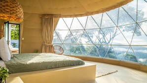 Una habitación amplia con una cama grande, un sillón colgante y vistas a través de una ventana de diseño geométrico.