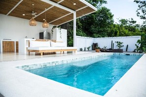 A modern outdoor pool area with a white pool, wooden deck, and a covered seating area with a sofa and hanging lights. - Magnificent Ocean view Glamping by BOTKa in Puerto Carrillo (Puerto Carrillo)