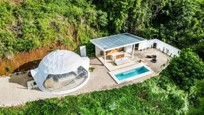 Una casa moderna con una estructura en forma de cúpula, piscina y patio rodeado de abundante vegetación.