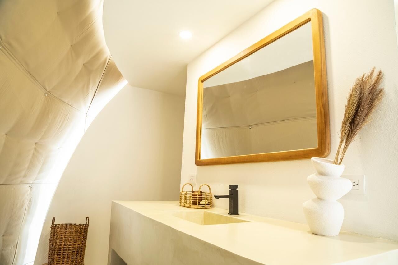 A bathroom with a large mirror, a white sink, a black faucet, a woven basket, and a white vase with dried plants.