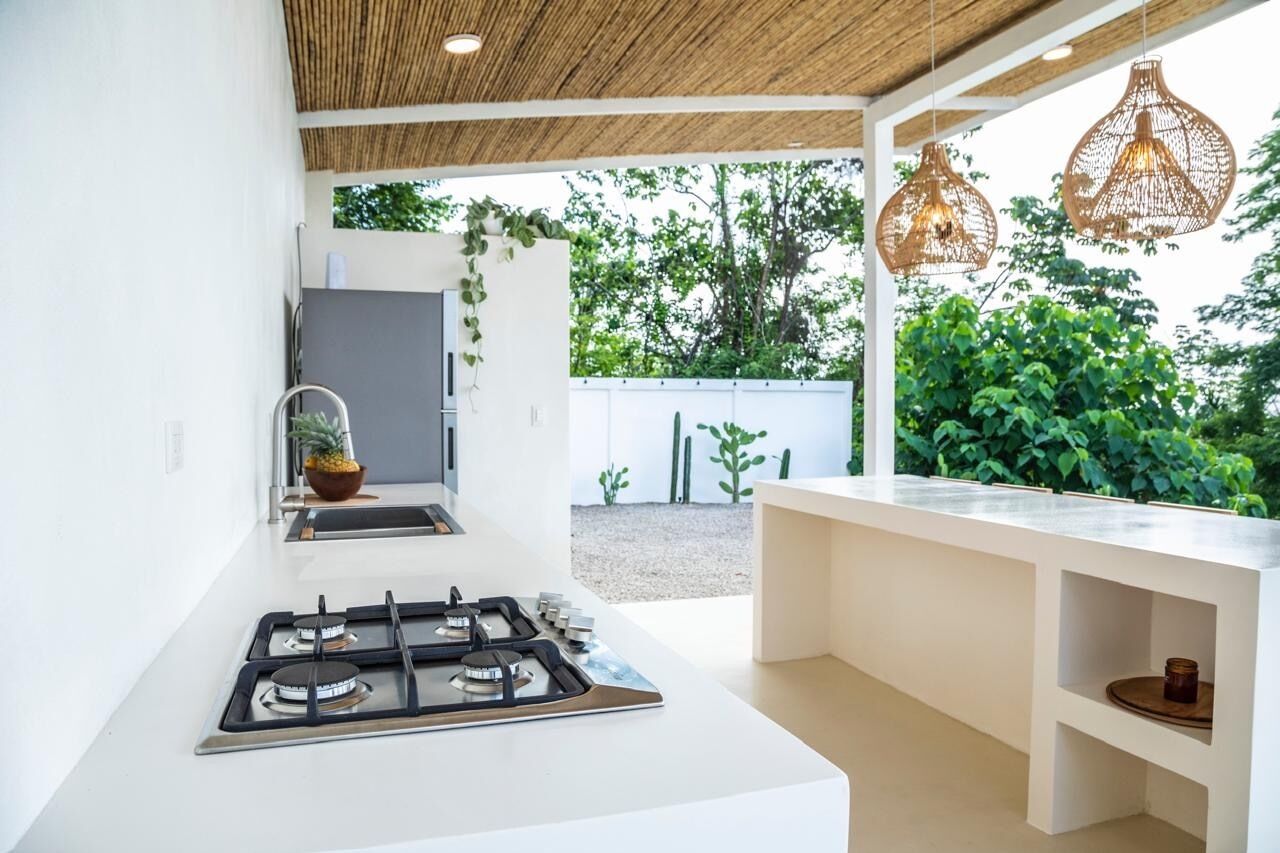 Een moderne keuken met een gasfornuis, witte kasten en hangende pendellampen.