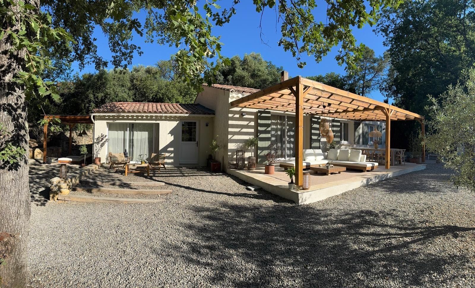 Ein Haus mit einer Terrasse, einem überdachten Sitzbereich und einem Schotterweg.