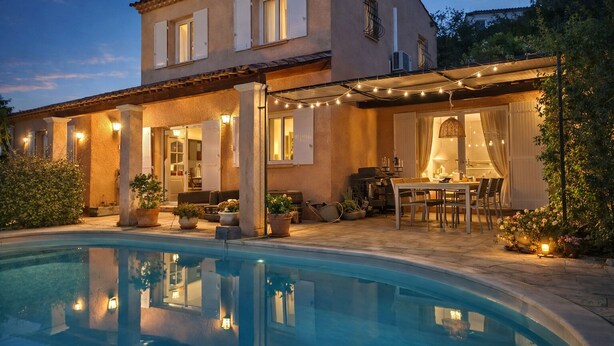 Ein zweistöckiges Haus mit Swimmingpool, Sitzbereich im Freien und Lichterketten.