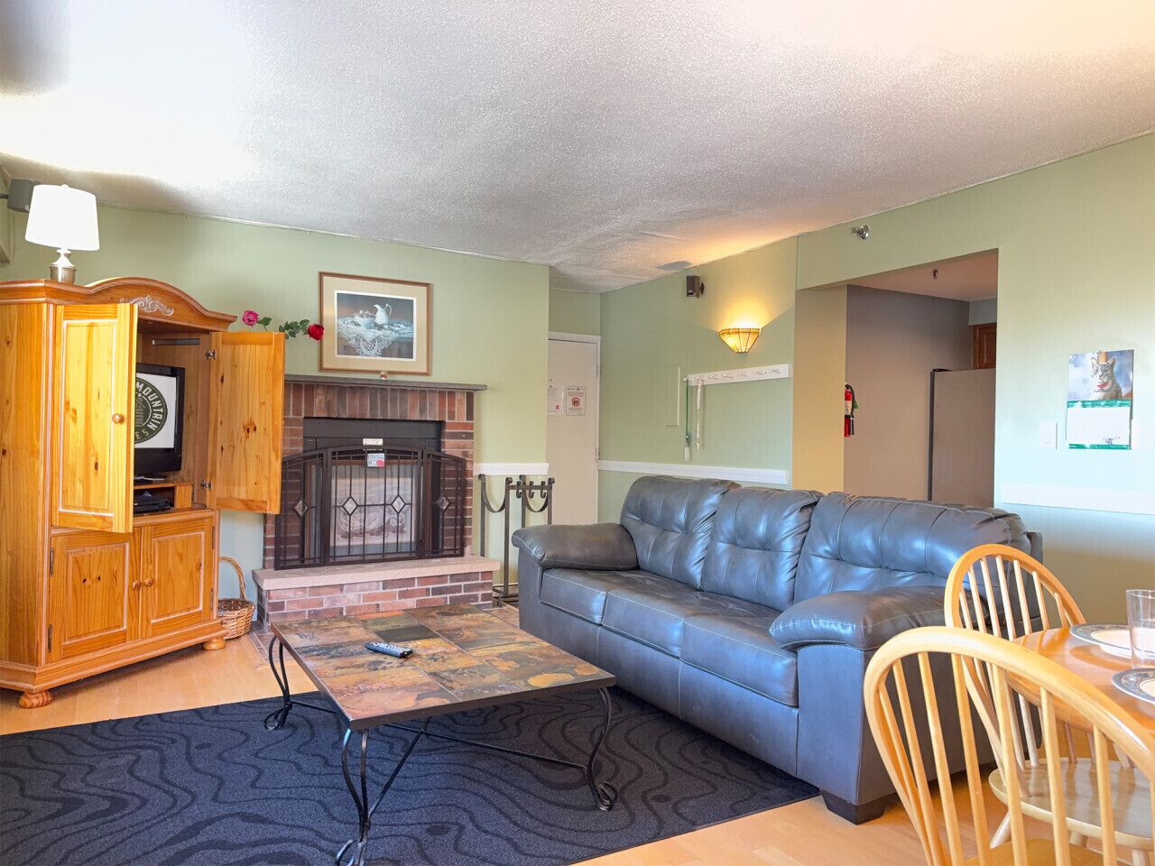 A living room with a fireplace, a leather sofa, a wooden cabinet, and a dining table with chairs.