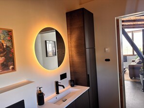 A modern bathroom with a large mirror, a white sink, a black faucet, and a wooden accent wall. - Valey Countryside Escape (Hvammstangi)