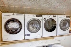 A row of four front-loading washing machines on a wooden shelf. - Valey Countryside Escape (Hvammstangi)