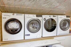 A row of four front-loading washing machines on a wooden shelf.