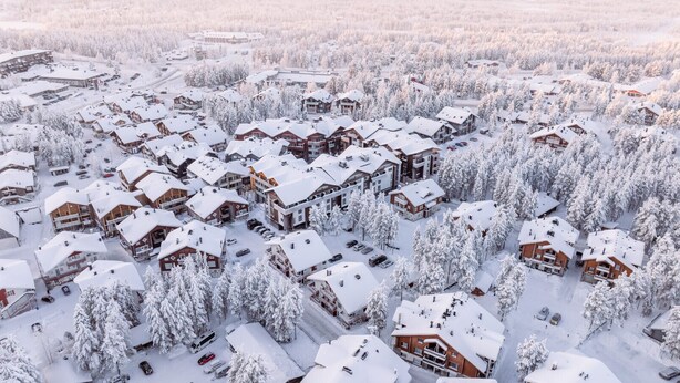 Et snedækket feriested med flere chalet-lignende bygninger, anlagt i en kompakt plan med synlige parkeringsområder og omgivet af tæt skov.