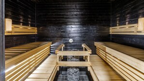 En sauna med træbænke og en midterbænk, stengulv og en sort trævæg.