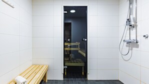 Um banheiro pequeno e revestido com azulejos, com um banco, chuveiro e porta para outro cômodo.