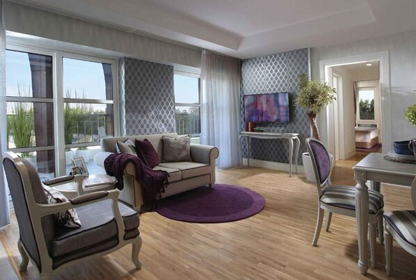 Una sala de estar moderna con sofá, sillones, una mesa de comedor y un ventanal que ofrece vistas a zonas verdes.