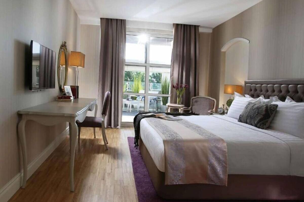 Habitación de hotel con cama, escritorio, silla, televisor y ventana con cortinas.