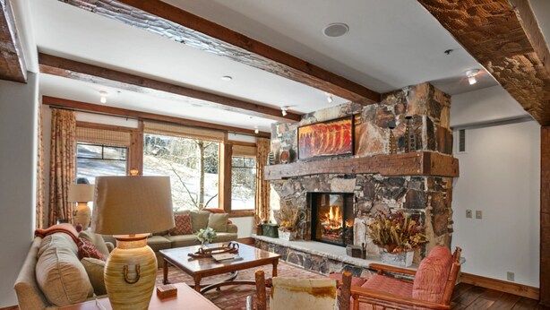 A cozy living room with a stone fireplace, wooden beams, and a large window. - Grand Lodge - 3 Bedroom Deluxe #404 - Ski-in/out 3 Condo (Park City)