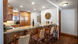 A kitchen with wooden cabinets, a granite countertop, and a large clock on the wall. - Grand Lodge - 3 Bedroom Deluxe #404 - Ski-in/out 3 Condo (Park City)