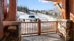 A wooden deck with a stone wall and a view of a snowy landscape with a ski lift. - Grand Lodge - 3 Bedroom Deluxe #404 - Ski-in/out 3 Condo (Park City)