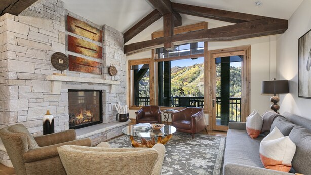 A cozy living room with a stone fireplace, leather sofas, and a view of a mountainous landscape through large windows. - Ski-in/ski-out Deer Valley Escape 2 Bedroom Condo (Park City)