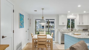 A modern kitchen with white cabinets, a marble countertop, and a dining area with a wooden table and chairs. - Gsr9220 2 Bedroom Home (Englewood)