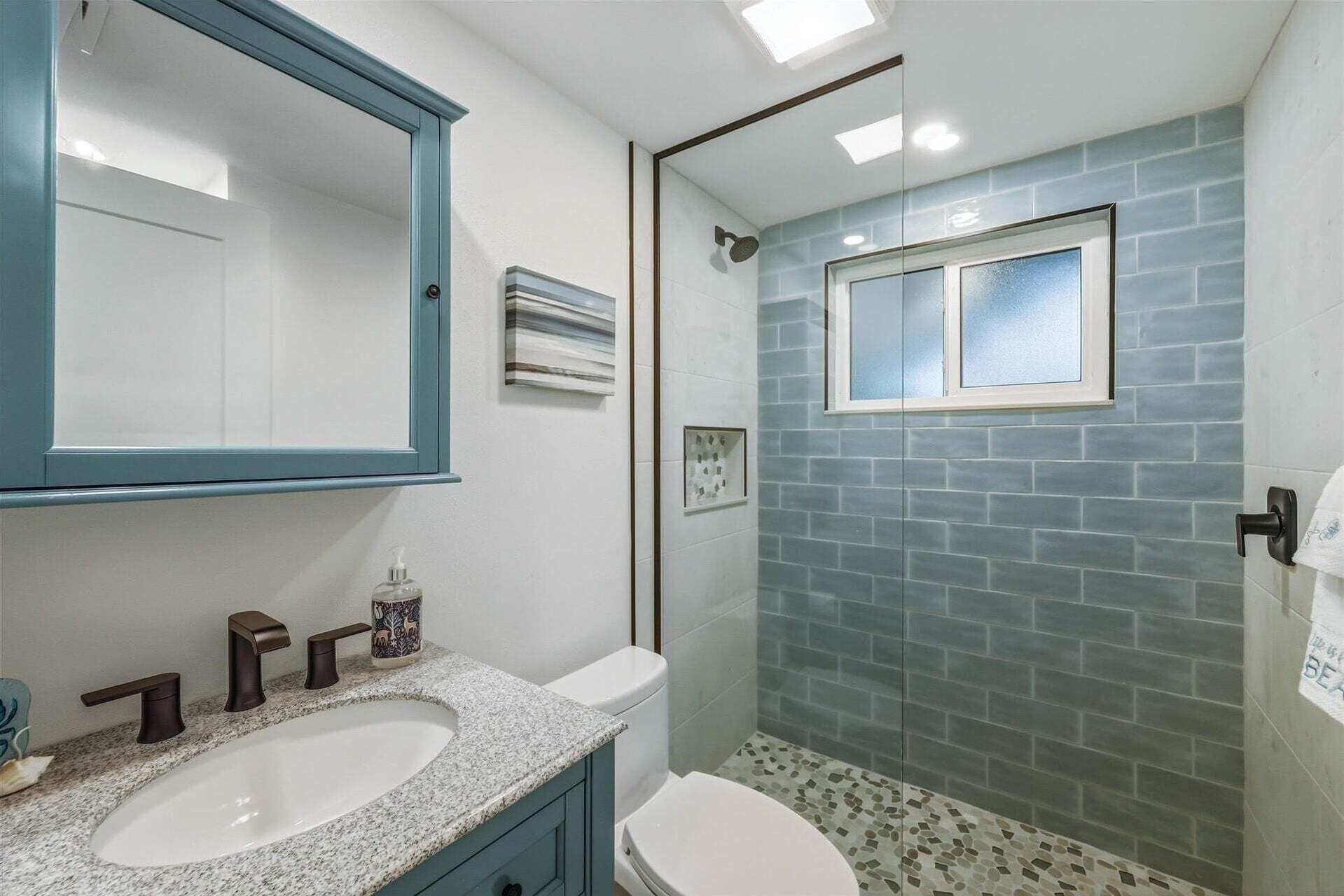 Baño con lavamanos doble, inodoro, ducha con puerta de vidrio y espejo con marco azul.