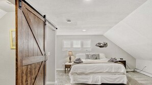 A bedroom with a large wooden door, a bed with white bedding, a nightstand, a lamp, and a wall decal. - Black Hawk Getaway W/ Hot Tub 3 Bedroom Cabin (Black Hawk)