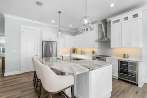 A modern kitchen with white cabinetry, a marble island, pendant lighting, and a built-in oven. - 5960 Sunset Beach: 4br Beachfront Home W/ Pool! 4 Bedroom Home (Fort Myers Beach)
