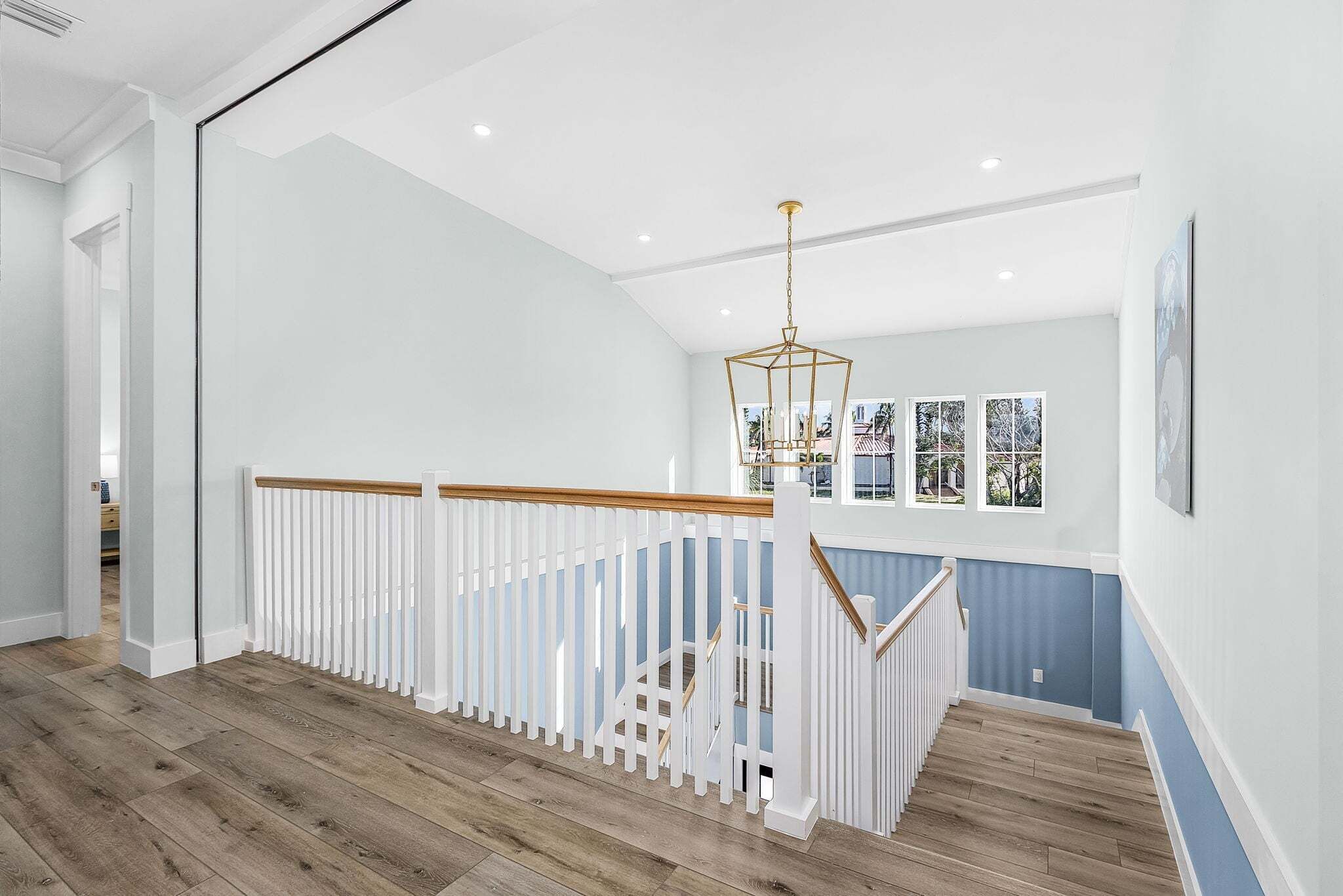 Un interior amplio con una escalera de madera, barandillas blancas y una lámpara moderna.