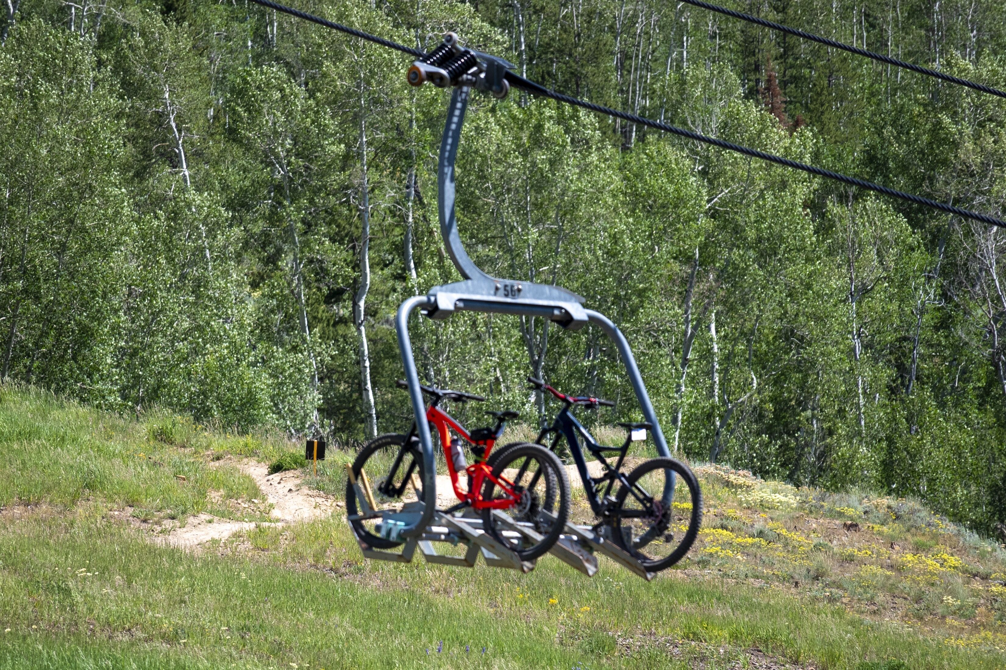 A chairlift with two bicycles attached, set against a forested hillside.