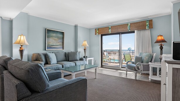 A spacious living room with a large sofa, a glass coffee table, and a view of the ocean through a sliding glass door. - Ocean One 213 - Second Floor Oceanfront 3BR Condo (Hilton Head Island)