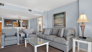 A living room with a grey sofa, two armchairs, a glass coffee table, and a lamp on a side table. - Ocean One 213 - Second Floor Oceanfront 3BR Condo (Hilton Head Island)