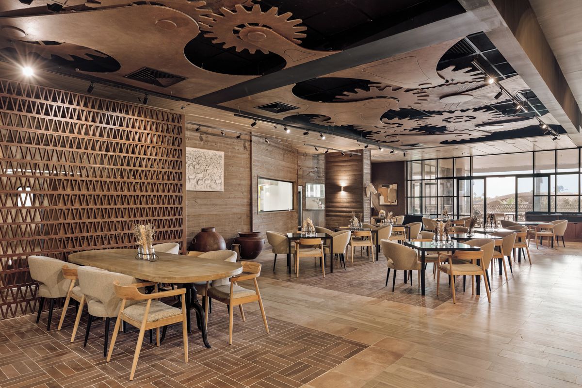 Un comedor amplio con varias mesas y sillas, piso de madera y un techo decorativo con diseños de engranajes.