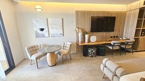 Un salon moderne avec une table ronde, deux canapés, un téléviseur fixé à un mur en bois et un coin repas comprenant des chaises et une petite table.