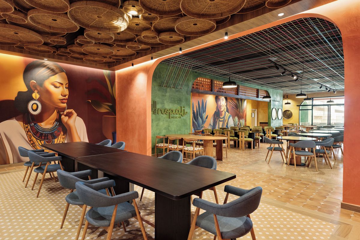 A spacious dining area with multiple tables and chairs, a mural on the wall, and a ceiling with a unique woven design.