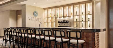 Zona de bar con mostrador, varios taburetes y una pared con botellas.