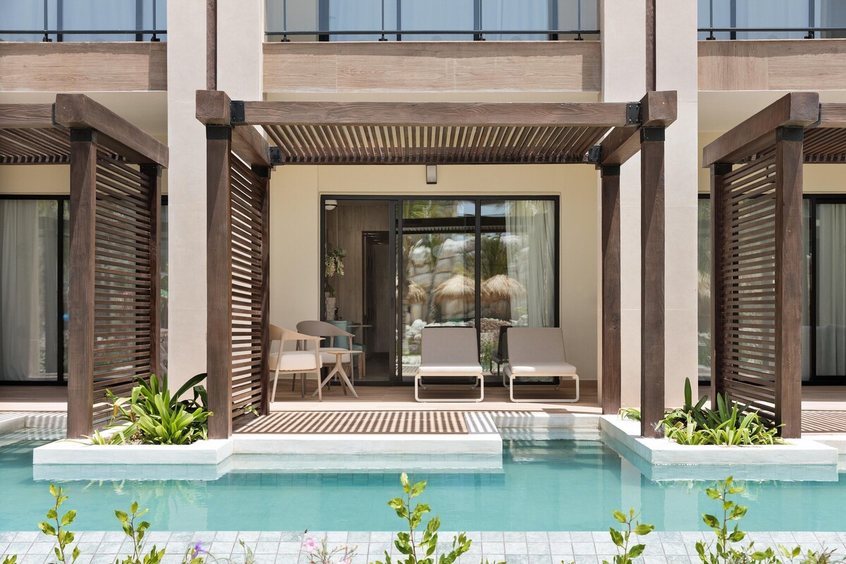 A poolside area with a pergola, lounge chairs, and a view into the building.
